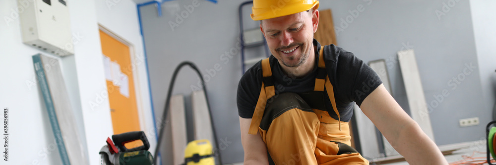 Happy carpenter places laminate panels on floor. Man gives instructions for laying substrate and laminate. Simplicity in installation floor material. Serial connection one board with another Happy carpenter places laminate panels on floor. Man gives instructions for laying substrate and laminate. Simplicity in installation floor material. Serial connection one board with another