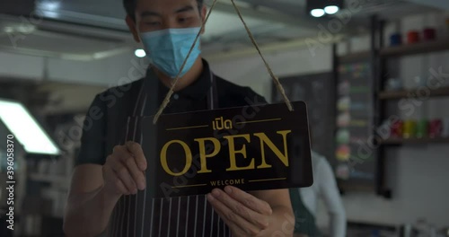 Asian man business owner in safety mask hanging up sign with inscription closed on cafe door. Waitress in protective mask closing restaurant because of pandemic.