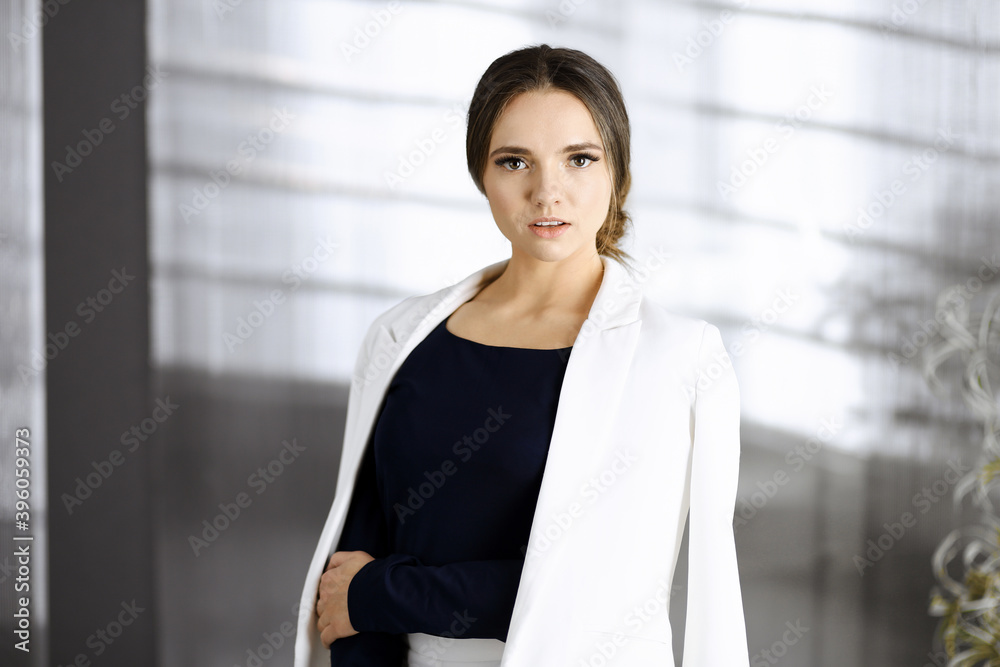 Friendly young business woman or female student dressed in white suit is standing straight and posing at camera. Lifestyle and diverse people concept