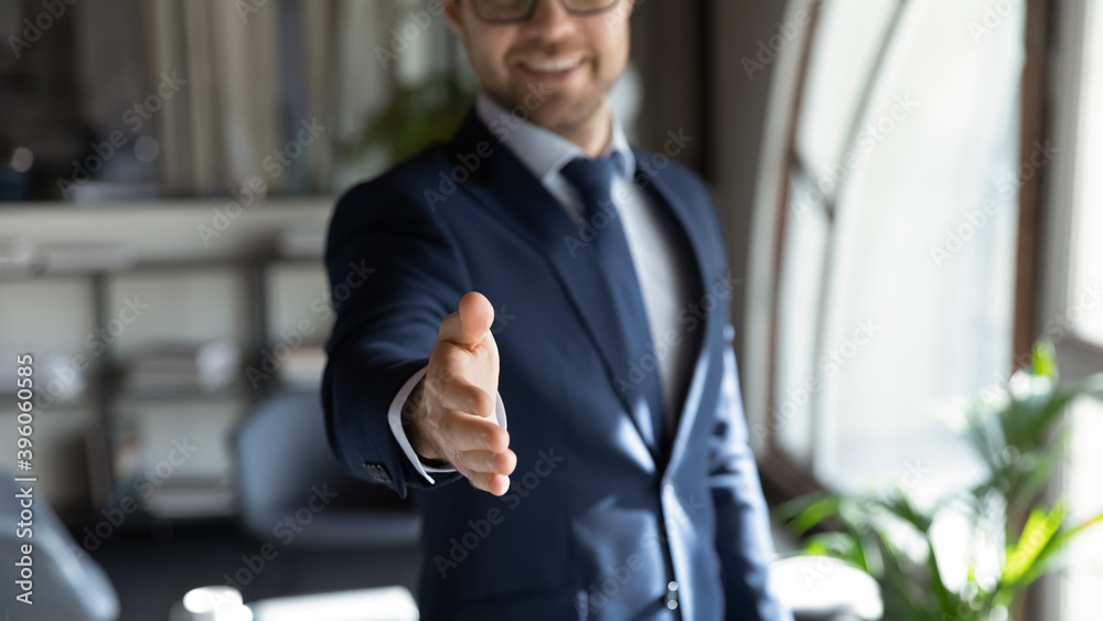 © fizkes - Close up cropped portrait of smiling successful friendly young man in formal attire hr recruiter stretching hand to camera glad to offer you job in company, greeting spectator as new workforce member