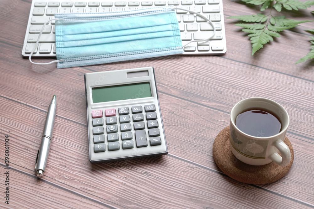 Wood table with keyboard, face mask, coffee, pen, calculator and green plants. Wood table with keyboard, face mask, coffee, pen, calculator and green plants.
