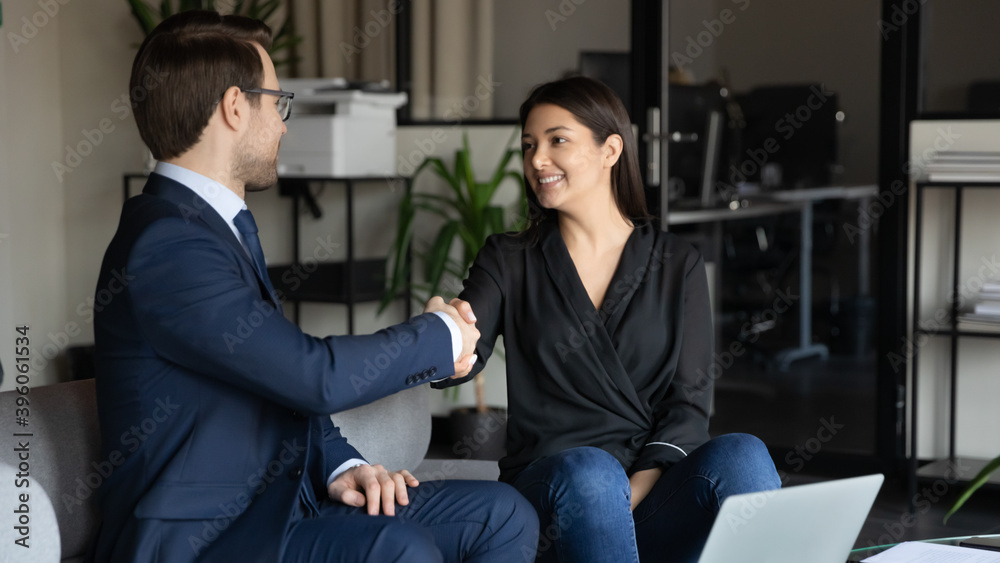 Thank you for help. Happy smiling young mixed race woman client customer shaking hand of millennial man real estate broker insurance agent bank manager grateful for help signing agreement making deal