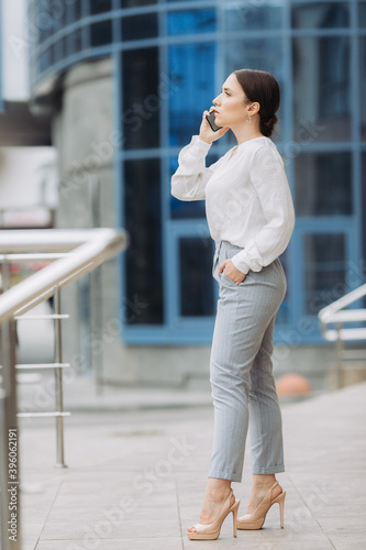 A business woman walking down the street in a business district talking on the phone.