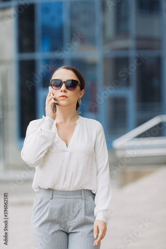 A business woman walking down the street in a business district talking on the phone.