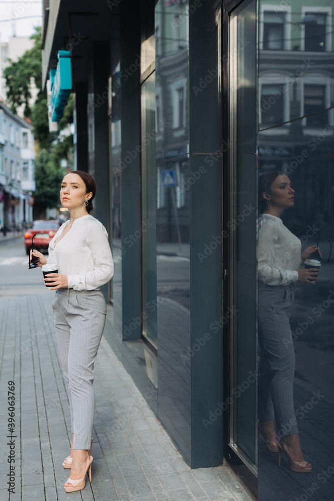 Shot of smiling young business woman using her mobile phone while drinking coffee walking down the street.