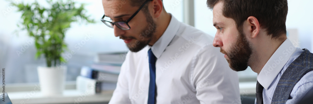 Attentive bearded male person sitting in front of computer and being in all ears while making notes