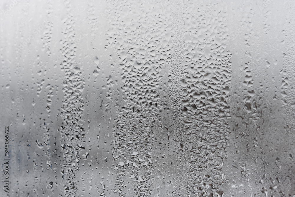 Natural drops of water flow down the glass, high humidity in the room, condensation on the glass window. Neutral colors. Excellent background with condensation drops texture Natural drops of water flow down the glass, high humidity in the room, condensation on the glass window. Neutral colors. Excellent background with condensation drops texture