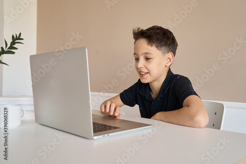 Schoolboy boy sitting at a desk with a laptop, writes school lessons during homework. High quality photo