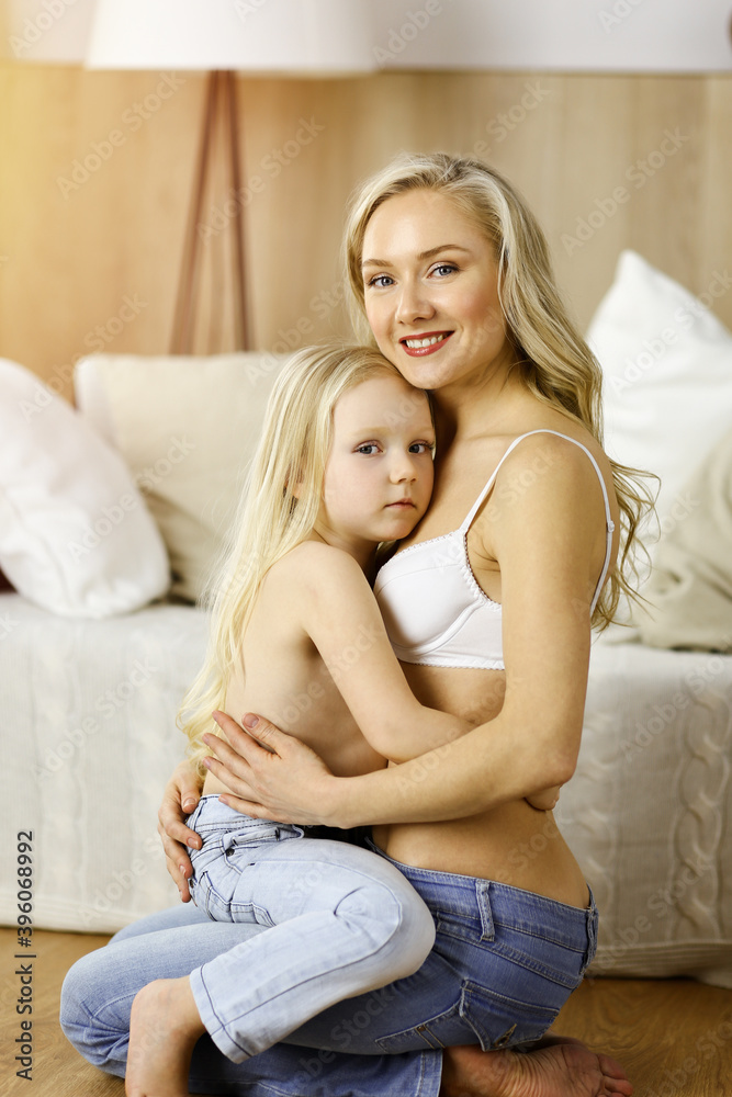 Happy mom and little daughter cuddle while dressing in sunny room. Motherhood and family concept Happy mom and little daughter cuddle while dressing in sunny room. Motherhood and family concept