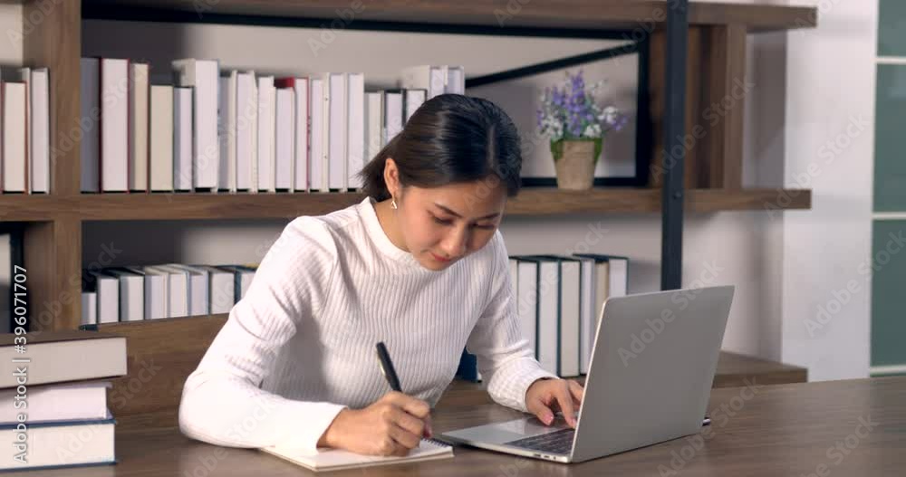 Asian woman using laptop in coffee shop with barista on background. Female freelancer communicates with someone and typing on computer. Asian woman using laptop in coffee shop with barista on background. Female freelancer communicates with someone and typing on computer.