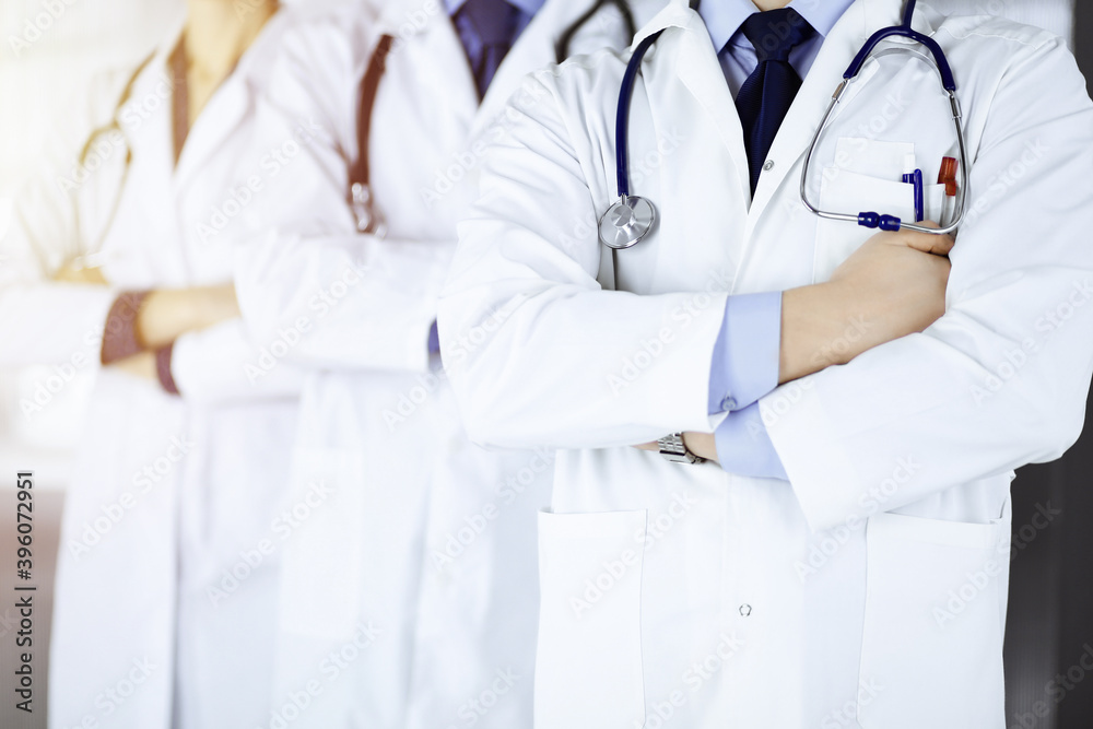 Group of modern doctors standing as a team with crossed arms and stethoscopes in a sunny hospital office. Physicians ready to examine and help patients. Medical help, insurance in health care, best