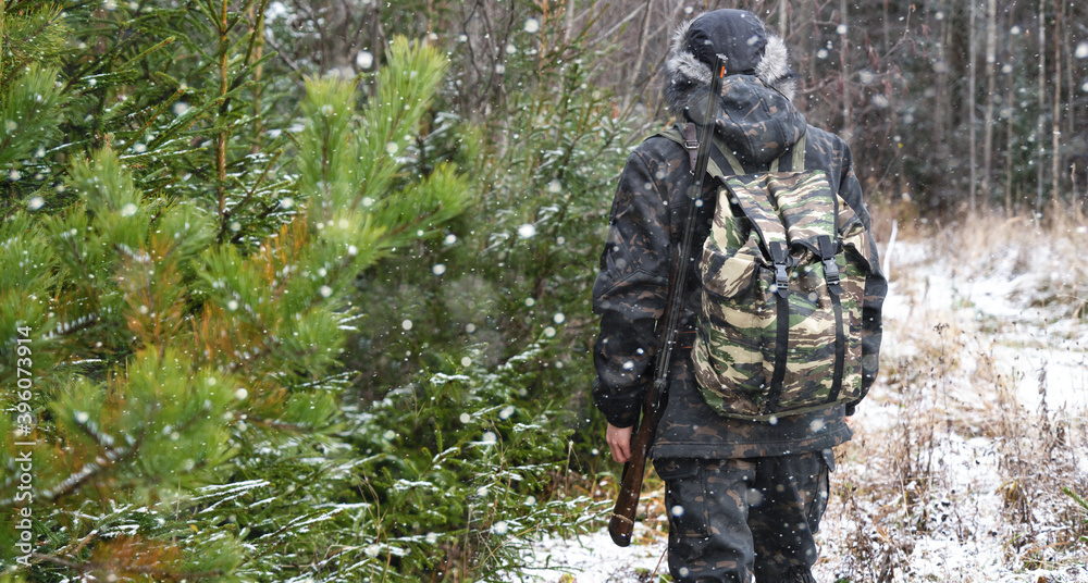 Hunter with a gun and a backpack in the winter forest	
