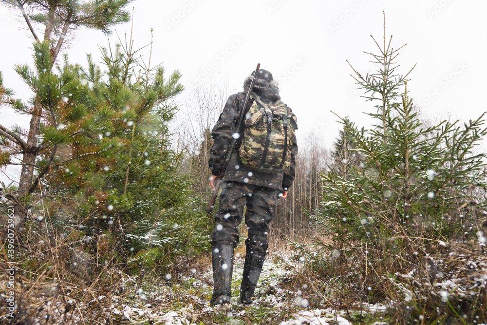 Hunter with a gun and a backpack in the winter forest	
