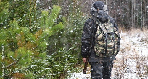 Hunter with a gun and a backpack in the winter forest 