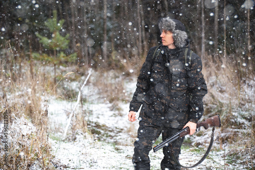 Hunter with a gun and a backpack in the winter forest 