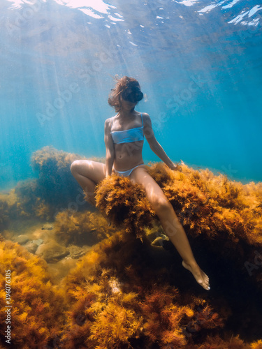 Attractive woman posing and sitting at sea bottom underwater. Freediver in sea
