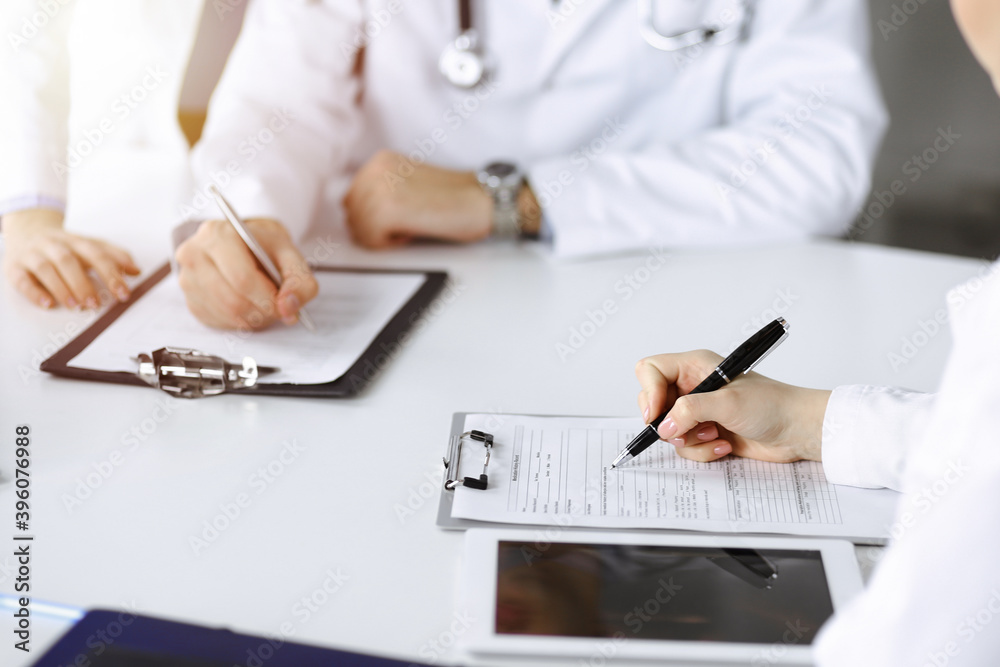 Group of unknown doctors are sitting at the desk and discussing problems or disease treatment in sunny hospital office. Covid 2019 Group of unknown doctors are sitting at the desk and discussing problems or disease treatment in sunny hospital office. Covid 2019