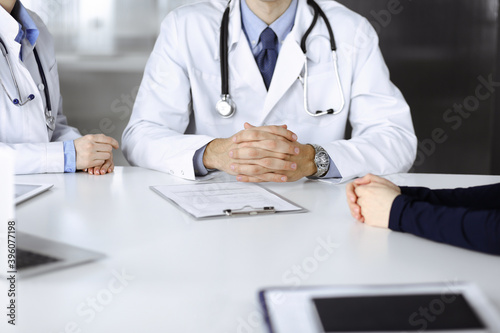 Unknown male doctor listening to his patient woman while sitting in modern clinic. Perfect medical service, medicine concept during Coronavirus pandemic. Covid 2019
