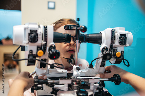 Beautiful and adorable little girl receiving ophthalmology treatment. Doctor ophthalmologist checking her eyesight with modern equipment.