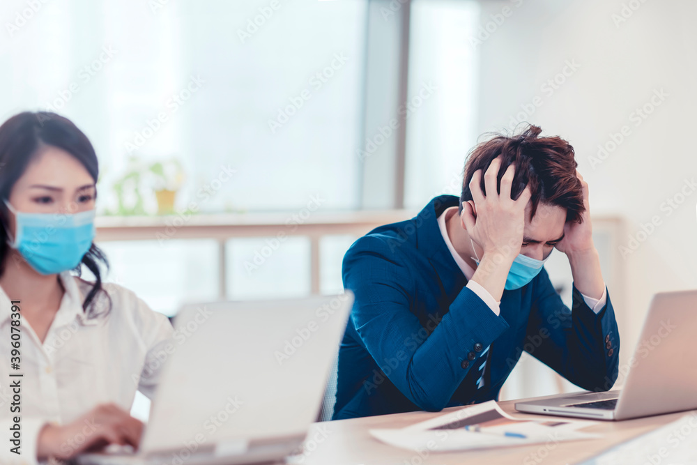 Stressed business man wear face mask and working on laptop in office Stressed business man wear face mask and working on laptop in office
