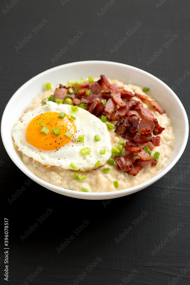Homemade Cheesy Bacon Savory Oatmeal Bowl on a black background, side view. Close-up.