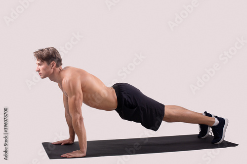 Full length portrait of strong young man standing in plank over light studio background, empty space
