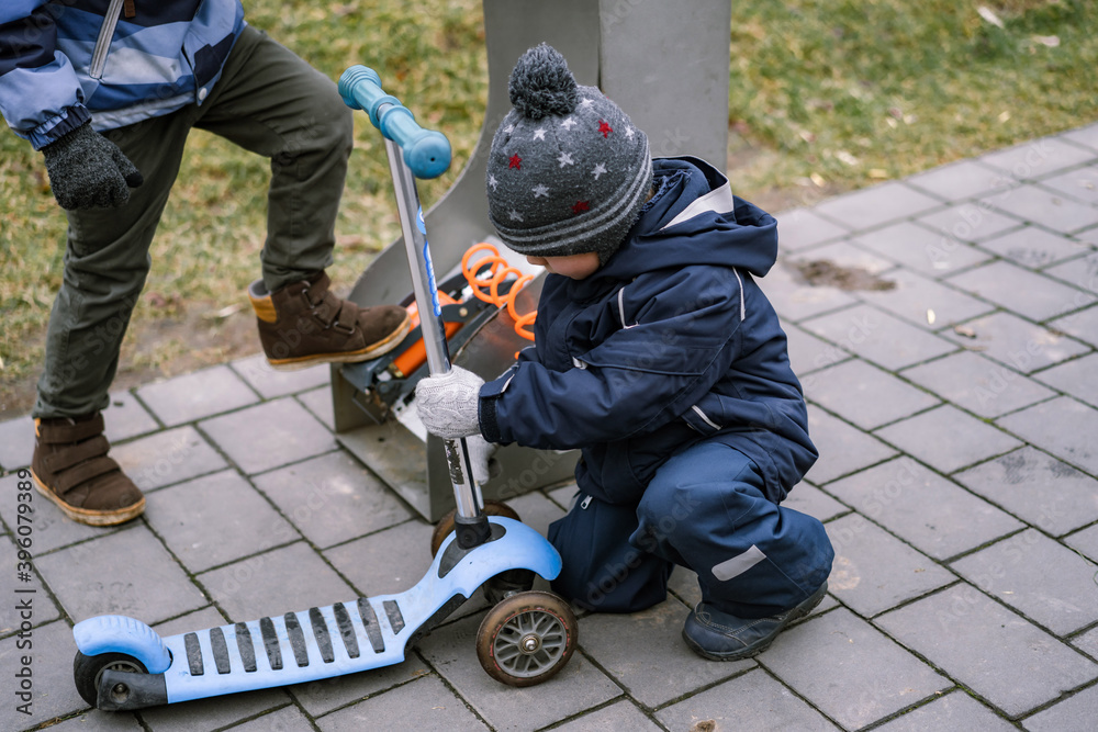 little boys pumping up a tire of their kick scooters with foot pump self service in the street, sitting on pavement little boys pumping up a tire of their kick scooters with foot pump self service in the street, sitting on pavement