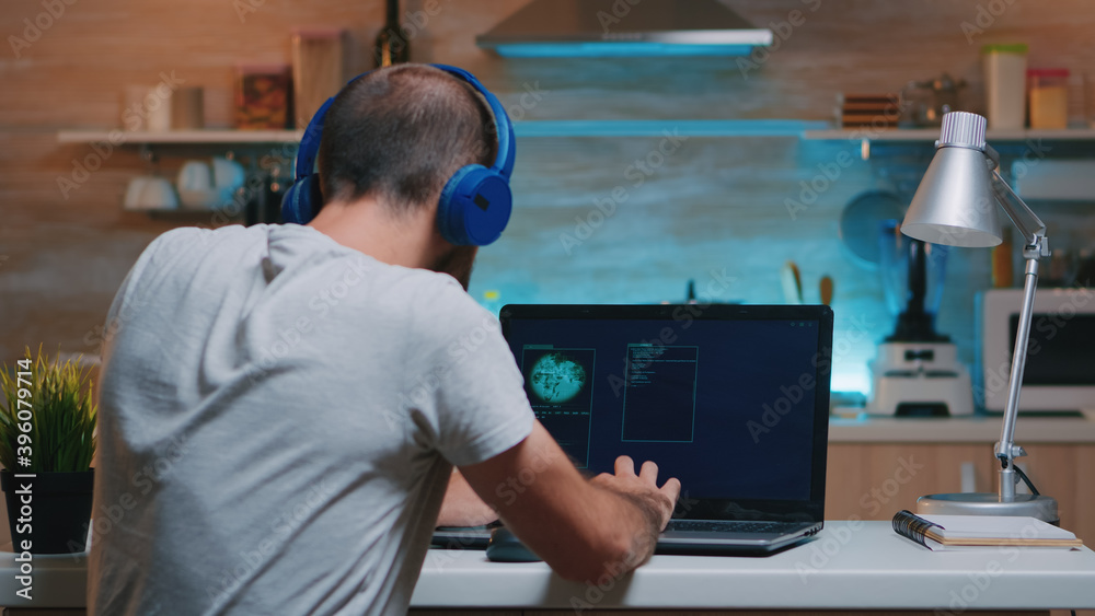 Remote man thief with headset stealing data from company hacking system from home. Programmer writing a dangerous malware for cyber attacks using performance device during midnight. Remote man thief with headset stealing data from company hacking system from home. Programmer writing a dangerous malware for cyber attacks using performance device during midnight.