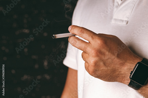 Male hand holding lit cigarette against black background
