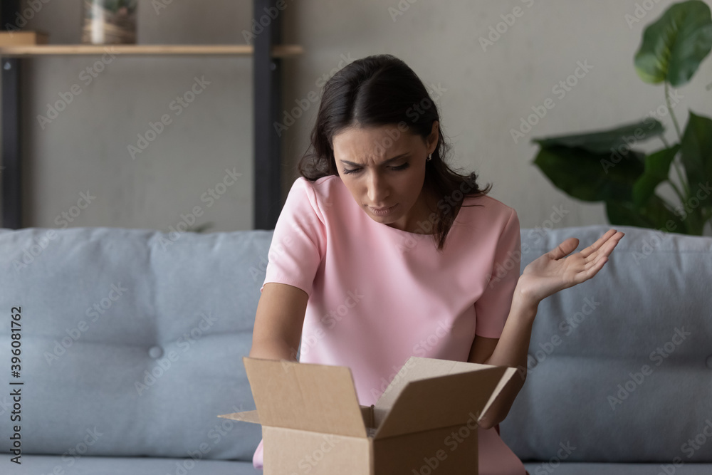 Unhappy young indian arabic ethnicity woman looking inside cardboard parcel, feeling displeased of getting crashed item product or receiving wrong order, negative online shopping experience. Unhappy young indian arabic ethnicity woman looking inside cardboard parcel, feeling displeased of getting crashed item product or receiving wrong order, negative online shopping experience.