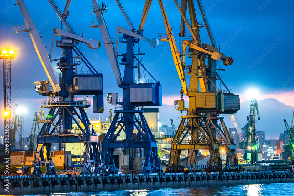 Sea ports view from sea. Several loading cranes at seaport. Installations for loading in seaport. Tower cranes at the cargo port. Marine loading terminal on background of the evening sky. Sea ports view from sea. Several loading cranes at seaport. Installations for loading in seaport. Tower cranes at the cargo port. Marine loading terminal on background of the evening sky.