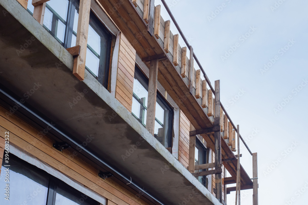 Fragment of a house under construction. Unfinished house is sheathed with wood. Facing house with wooden beams. Fragment of a building on sky background. Construction of a two-story cottage
