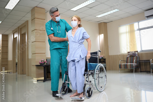 Doctor or assistance staff wear face mask and help or assist an elder patient woman while try to standing or walking or sitting on wheelchair in the hospital, eldercare concept