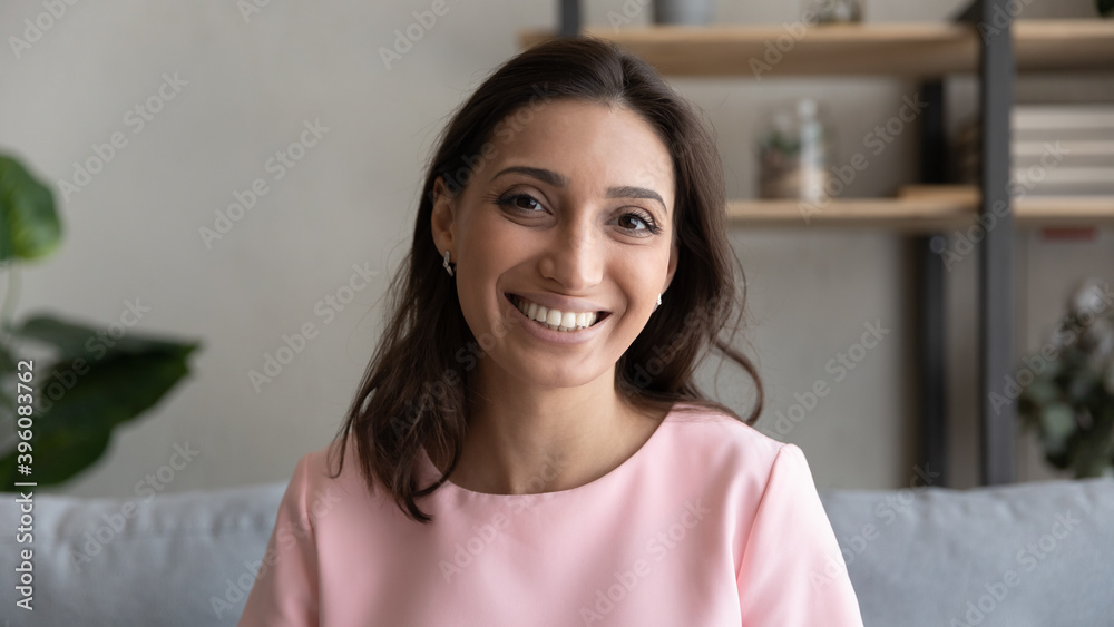 Web camera head shot computer screen view smiling mixed race arab indian woman sitting on sofa, holding video call internet meeting, passing distant job interview or communicating remotely online.