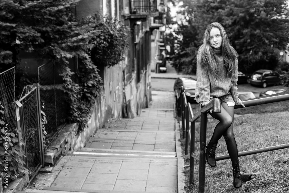 Obraz premium Young long-haired girl sitting on the parapet in the old town. Black and white photo.