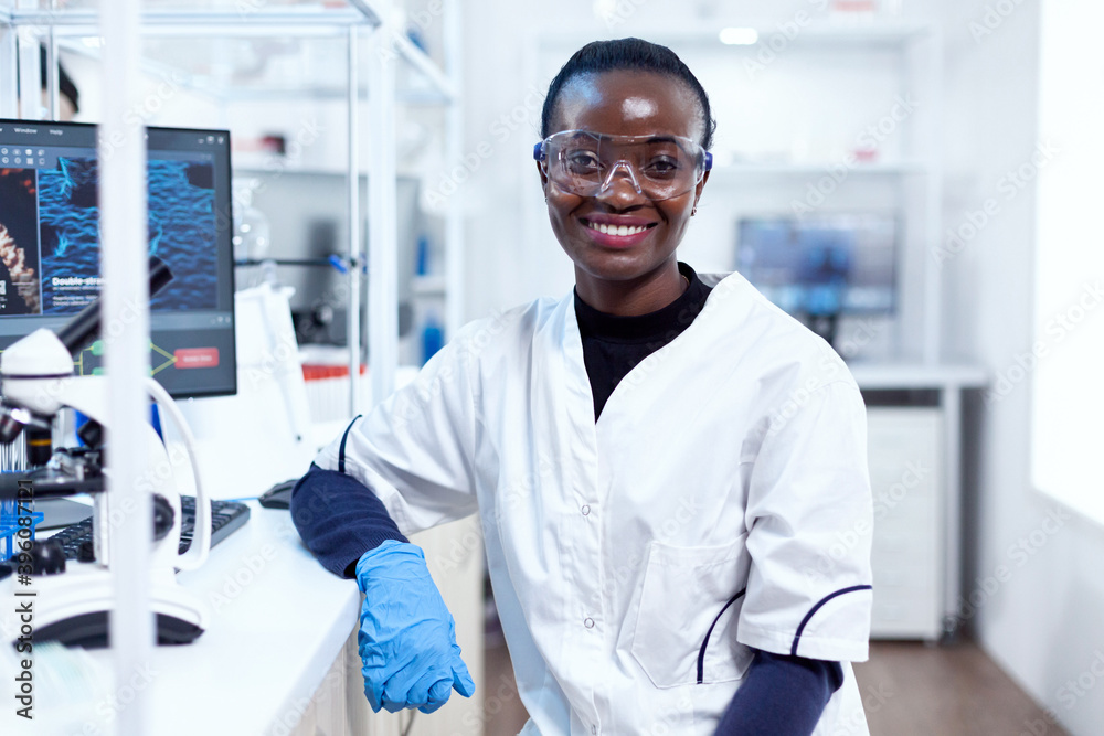 Portrait of professional african scientist smiling at camera in sterile laboratory. Multiethnic team of researchers working in microbiology lab testing solution for medical purpose. Portrait of professional african scientist smiling at camera in sterile laboratory. Multiethnic team of researchers working in microbiology lab testing solution for medical purpose.