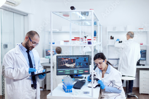Group of scientist doing health study using microscope and tablet pc. Team of researchers doing pharmacology engineering in sterile laboratory for healthcare industry with african assistant in the