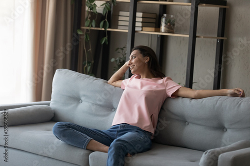 Relaxed young happy indian arab mixed race woman chilling on comfortable sofa in modern living room, breathing fresh air, dreaming visualizing future, enjoying stress free leisure time indoors.