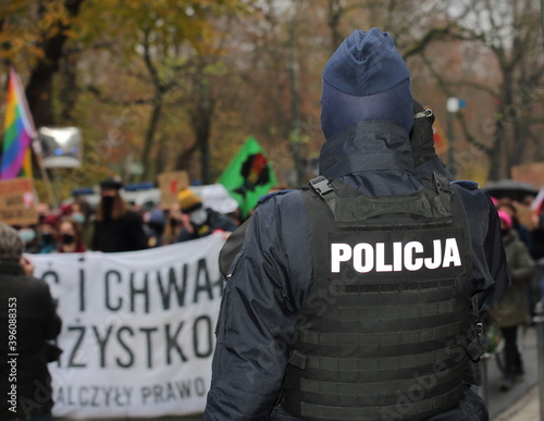Polish policeman in uniform on his back stands on street opposite of crowd of anti-government protesters organized by women strike movement
