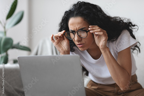 Young woman with bad eyesight using laptop, trying to work photo