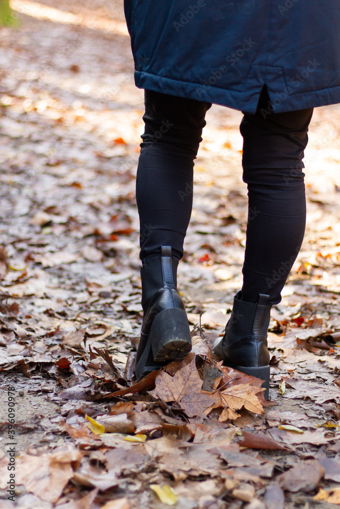 Girl in black pants, lifting the boot over the litter in the fall season