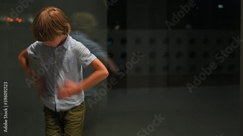 A lonely boy stands by a large window and cleans his clothes with the wind