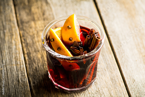 Mulled red wine with oranges and different spices in glass on the rustic background. Christmas food. Winter decorations. Selective focus. Shallow depth of field.