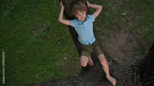 Boy lies on a large tree branch and shows his tongue