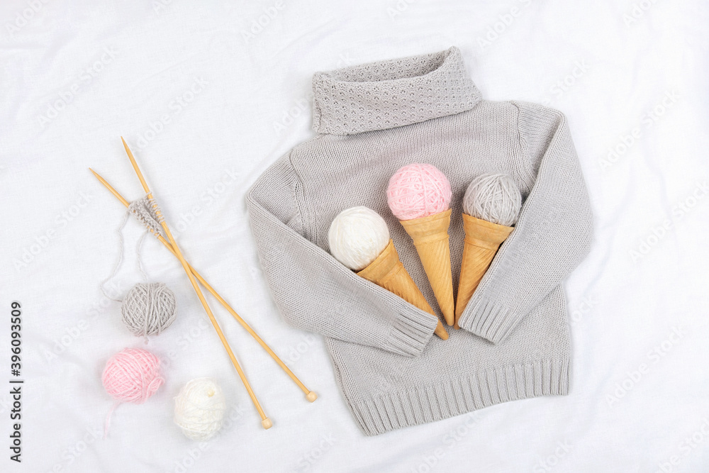 Three ice cream from yarn and waffle cones on a gray knitted sweater, wooden knitting needles on white background. Knitting, hobby and handmade concept. Top view Flat lay Three ice cream from yarn and waffle cones on a gray knitted sweater, wooden knitting needles on white background. Knitting, hobby and handmade concept. Top view Flat lay
