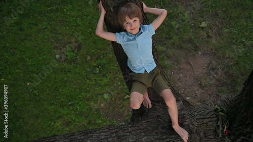 Boy laughs lying on a large tree branch over grass