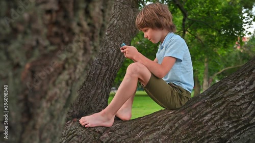 Boy emotionally plays on phone sitting on tree branch