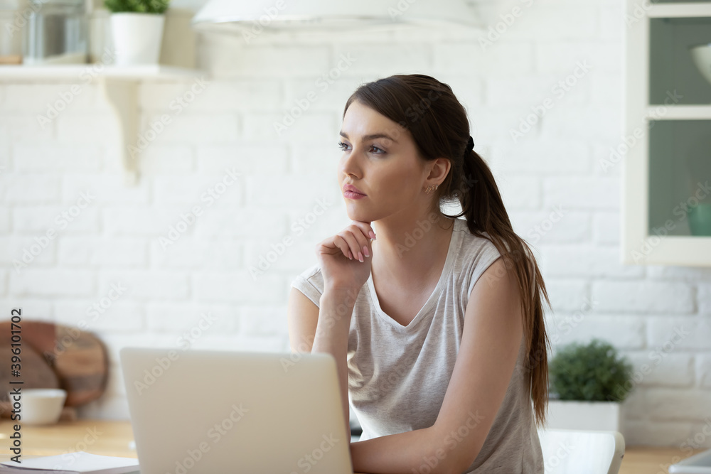 Dreamy thoughtful young woman sitting at table with laptop in kitchen, pensive female touching chin, pondering task, working or studying online at home, solving problems, visualizing Dreamy thoughtful young woman sitting at table with laptop in kitchen, pensive female touching chin, pondering task, working or studying online at home, solving problems, visualizing