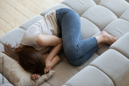 Top view unhappy depressed young woman lying on couch, sleeping, feeling unwell and unhealthy, frustrated sad female crying, suffering from divorce or break up, psychological problem