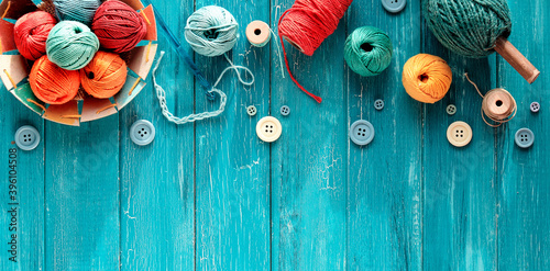 Decorative border made of wool bundles, yarn balls, buttons and cord. Latch and knitting needles. Creative flat lay, top view on distressed turquoise blue wood boards, copy-space, place for your text.